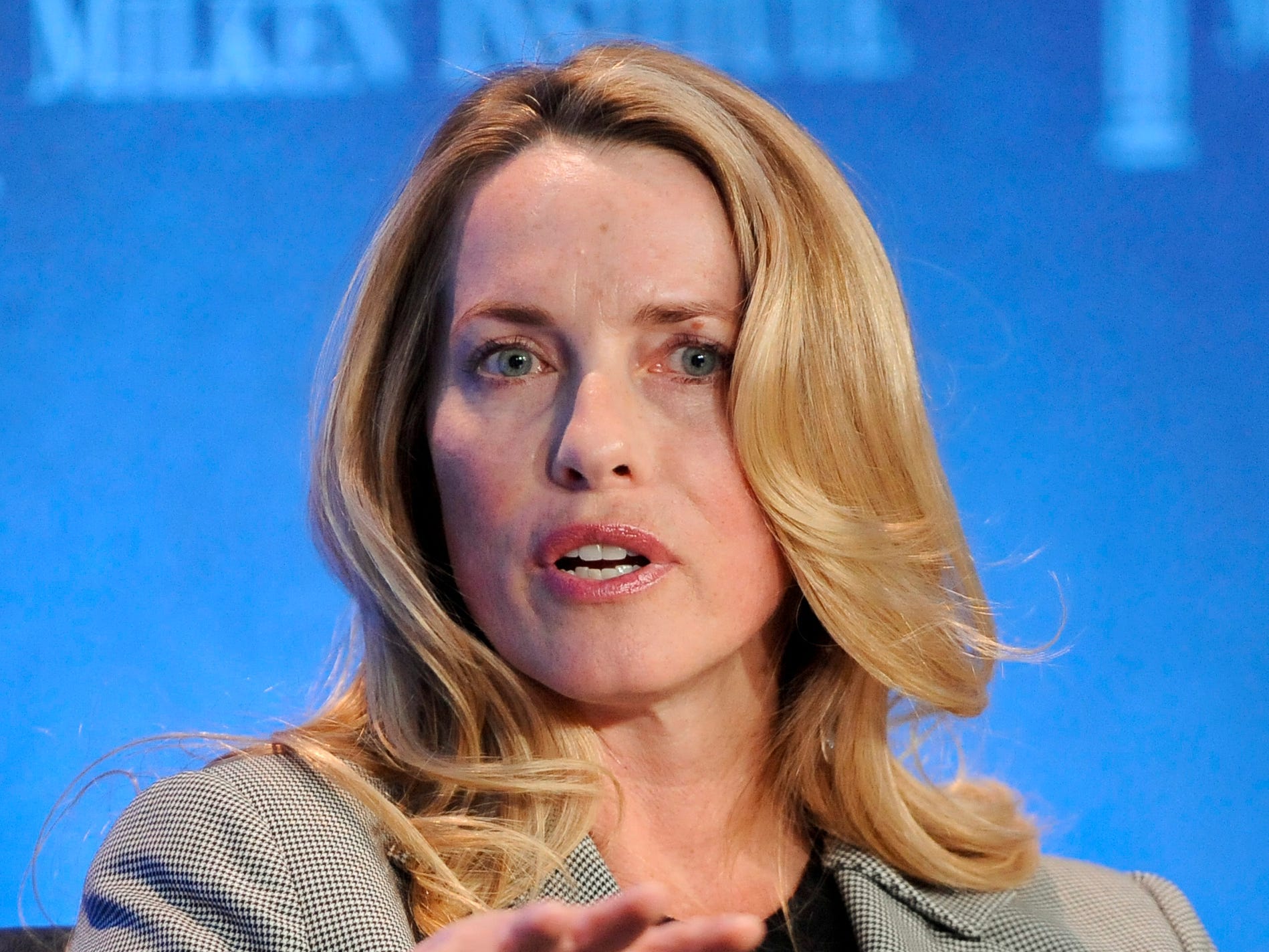 Laurene Powell Jobs dressed in a grey suit and talking on a stage, waves her hand forward to make a point