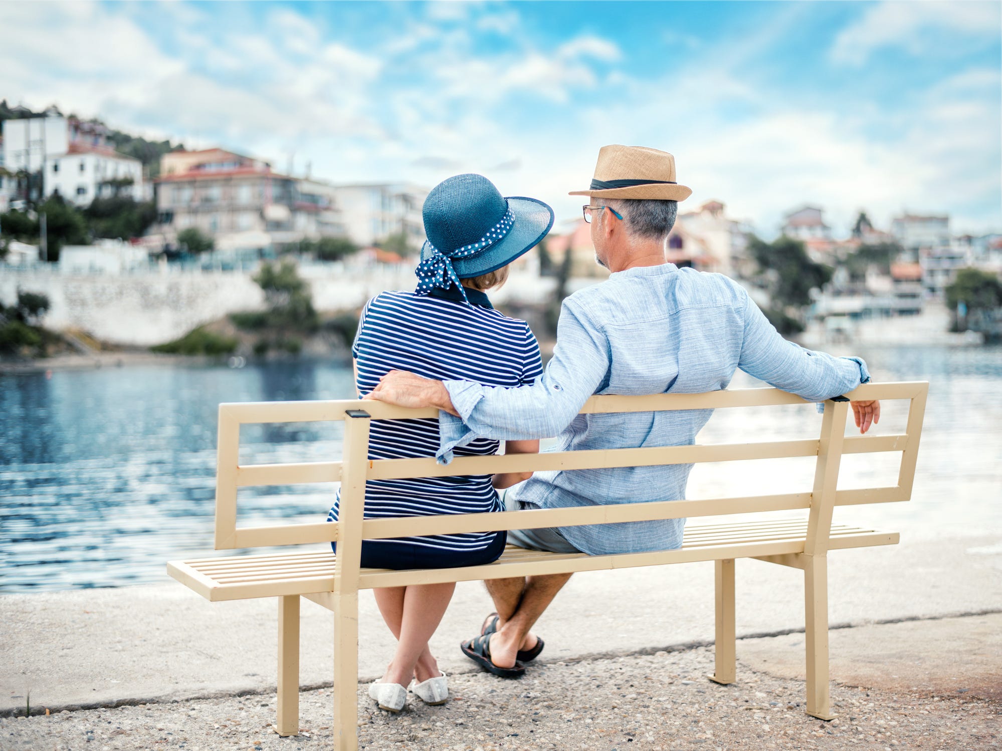 A stock photo of two people sitting on a bench and looking out onto the water.