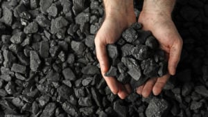 A man holds coal in his hands over a pile of more coal.