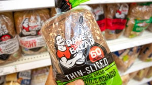 A hand holds a bag of Dave's Killer Bread at the grocery store