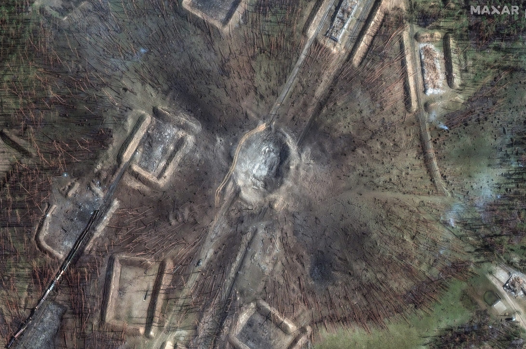 A large crater, downed trees, and destroyed railcars in a satellite image.