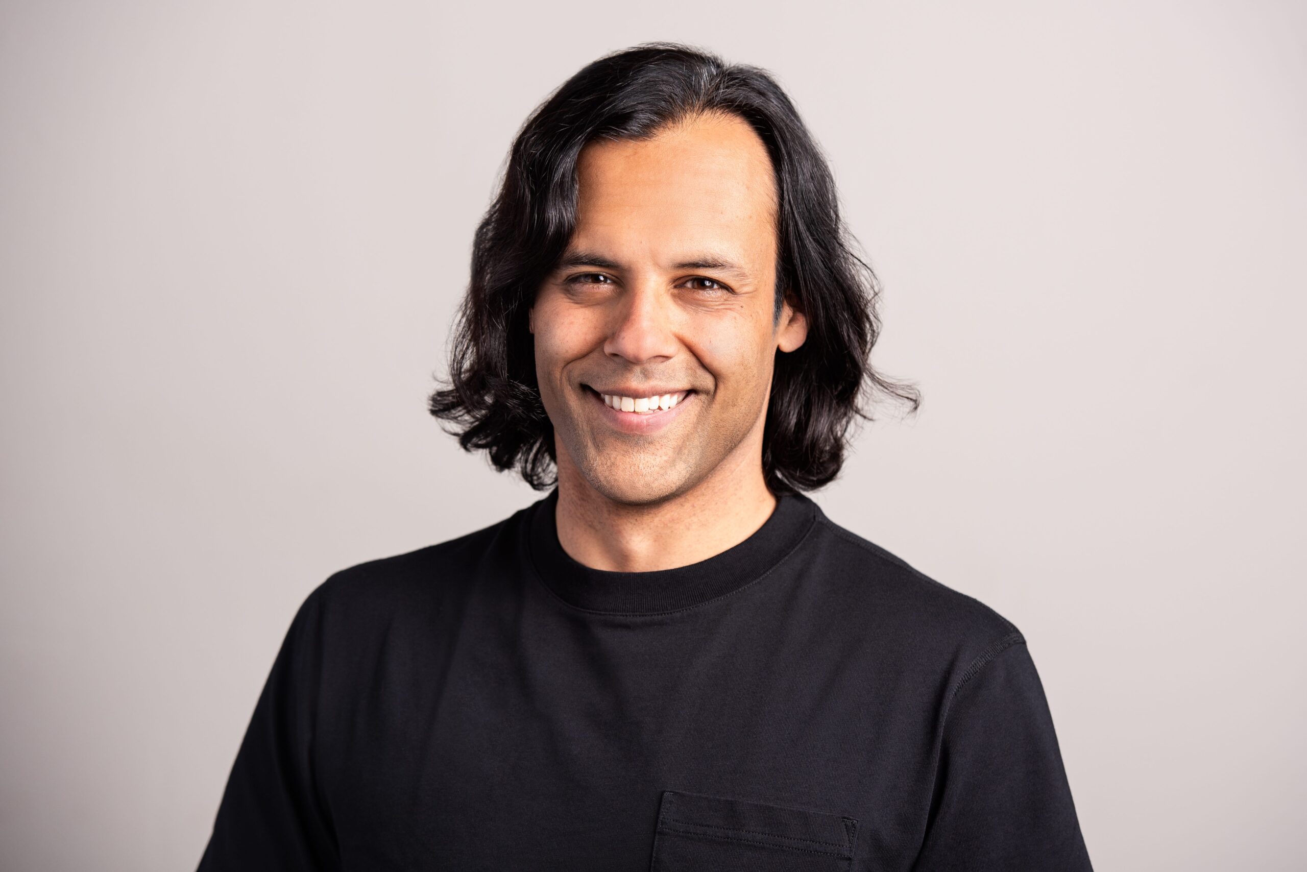 A profile of Baiju Bhatt smiling in a black t-shirt in front of a beige background.